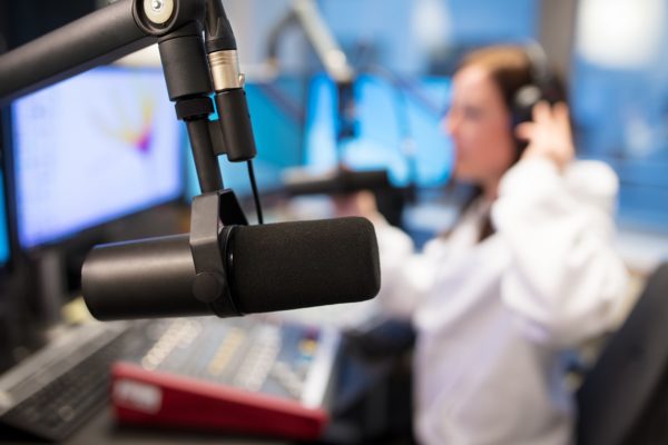 Młoda dziewczyna w słuchawkach siedzi przed konsolą w studiu nagrań